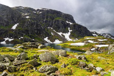 Snow is reflected in the icy water of the lake. Cold summer in Norway. Traveling by camper on road 520. Last year's snow and gray skies. 