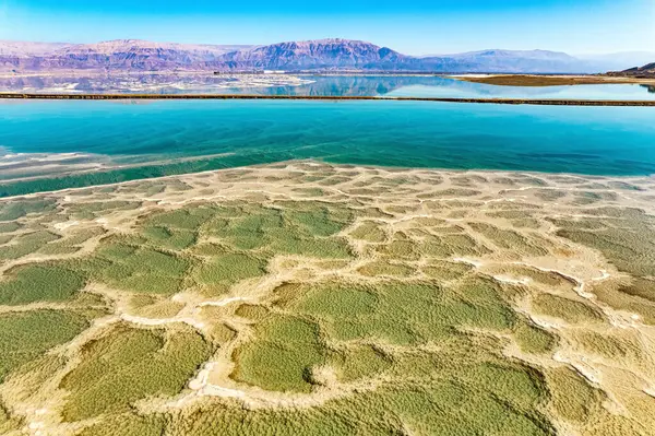 Dead Sea. The green water of the salty sea is surrounded by pink mountains. Salt deposits are visible on the seabed. Cold sunny winter day. Landscape photographed by a drone from a aerial view. Israel.