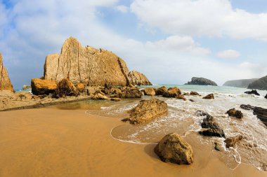 Resimli sahil kayalıkları. Playa de la Arnia plajındaki orijinal kaya çıkıntıları. Cantabria, İspanya. İnanılmaz jeolojik oluşumlar turistleri şaşırtır. Kar beyazı deniz köpüğü parlıyor 