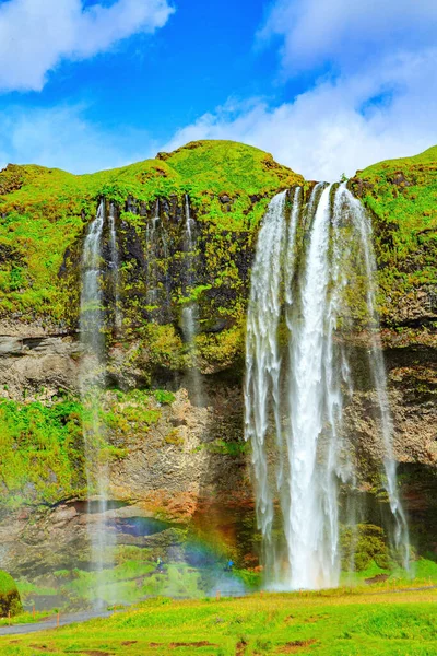 Travel to exotic Iceland. Magnificent rainbow appears in the splash of water. The famous Seljalandsfoss waterfall. Fine July day.