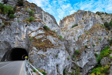 Asfalt karayolu dik kayaların arasından geçer ve bir tünelde kaybolur. Gün batımında aydınlanan gri kayalar. İspanya gezisi.. 