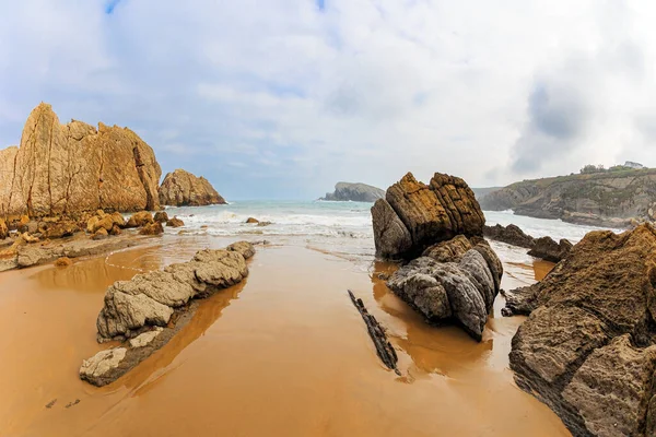 Playa de la Arnia sahilindeki tuhaf sahil kayalıkları. Cantabria, İspanya. İnanılmaz jeolojik oluşumlar. Kar beyazı deniz köpüğü parlıyor 