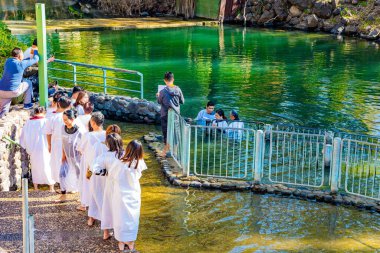 YARDENIT, ISRAEL - 21 HAZİRAN 2023: Vaftiz gömleği giyen neşeli hacılar Ürdün Nehri 'nin soğuk sularında vaftiz oluyorlar. Yardenit Hıristiyanların vaftiz merkeziydi. Güneşli kış günü. 