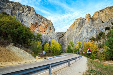 İspanya gezisi. Asfalt karayolu sarp kayalıkların arasından geçer. Gökyüzü ışık bulutlarıyla kaplı. Gün batımında parlayan büyük gri kayalar.