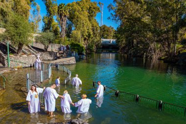 YARDENIT, ISRAEL - 21 HAZİRAN 2023: Vaftiz gömleği giyen neşeli hacılar Ürdün Nehri 'nin soğuk sularında vaftiz oluyorlar. Yardenit, Hıristiyanlar için bir vaftiz merkezi..