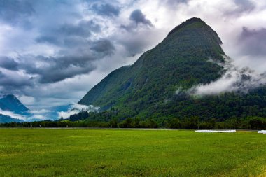 Yüksek orman dağlarıyla çevrili resimli bir vadi. Norveç 'te soğuk bir yaz. Çukurdaki yemyeşil çimenler. Ağır bulutlar gökyüzünü kapladı. Jostedalsbreen Parkı. 