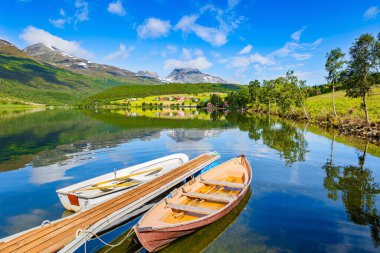 Tekneli ahşap iskele. Eidsvatnet Gölü. Norveç 'in merkezindeki resimli dağlar. Su yemyeşil bulutları, mavi gökyüzünü ve ormanlı kıyıları yansıtır. İskandinavya 'da yaz. 