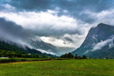 Ağır bulutlar gökyüzünü kapladı. Yüksek orman dağlarıyla çevrili resimli bir vadi. Çukurdaki yemyeşil çimenler. Jostedalsbreen Parkı. Norveç 'te soğuk yaz. 