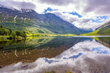 Su yemyeşil bulutları, mavi gökyüzünü ve ormanlı kıyıları yansıtır. İskandinavya 'da yaz mevsimi. Eidsvatnet - Norveç 'teki görkemli göl. Temiz şeffaf su ile derin göl
