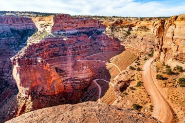 Kırmızı kumtaşından neredeyse dikey bir duvar yılansı bir yol ile kesişiyor. Utah, ABD 'deki Canyonlands Ulusal Parkı. Güneşli bir gün. Bir sürü vadi, dağ ve nehir vadisi var..