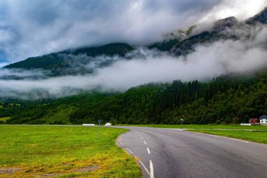 Geniş asfalt yol vadiyi geçer. Jostedalsbreen Parkı. Norveç 'te soğuk bir yaz. Yüksek orman dağlarıyla çevrili bir vadi. Yoğun bulutlar gökyüzünü kapladı. 