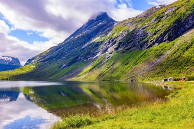 Norveç dağlarında Eidsvatnet Gölü sığ. İskandinavya 'da yaz mevsimi. Su yemyeşil bulutları, mavi gökyüzünü ve ormanlı kıyıları yansıtır.. 