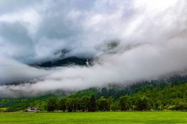 Ağır bulutlar gökyüzünü kapladı. Jostedalsbreen Parkı. Norveç 'te soğuk bir yaz. Yüksek orman dağlarıyla çevrili resimli bir vadi. Çukurdaki yemyeşil çimenler. 