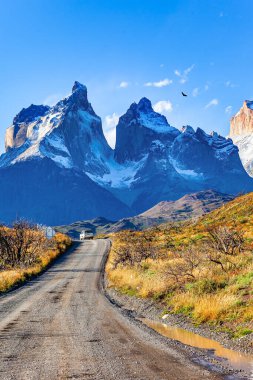 Los Cuernos 'un karla kaplı siyah uçurumları. Şilili Torres del Paine. Patagonya. Tepeler arasındaki toprak yol. Güney Şili 'ye destansı yolculuk. 