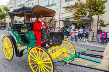 SAN FRANCISCO, ABD - 11 Ekim 2009: Kırmızı karnaval kostümlü yaşlı kadın iki atın çizdiği eski bir arabaya biniyor. Columbus Günü 'nün onuruna binicilik geçidi 