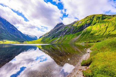 Su yemyeşil bulutları, mavi gökyüzünü ve ormanlı kıyıları yansıtır. Eidsvatnet - Norveç 'teki görkemli göl. Temiz şeffaf suyu olan derin bir göl. İskandinavya 'da yaz. 