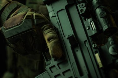 Eldivenli bir askerin taktik tüfeği sıkıca kavrayışını gösteren yakın plan bir görüntü. Dokuma eldivenlerine ve askeri sınıf silaha odaklanıldığında hassasiyet, hazırlık ve savaşın dayanıklı doğası vurgulanır..