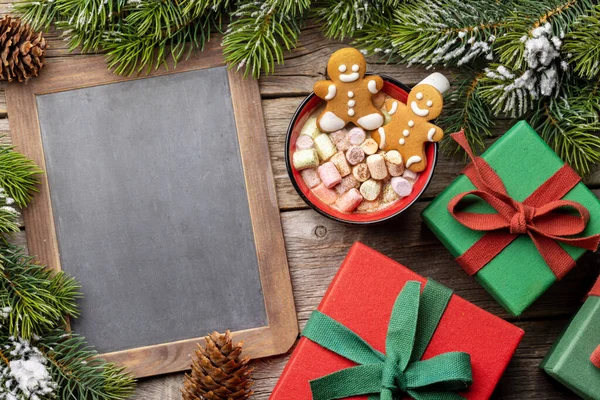 ジンジャーブレッドマンはマシュマロ入りのカップにクッキーを入れます コピースペースのための黒板とクリスマス休暇 — ストック写真