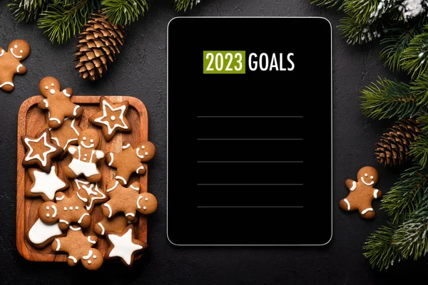 Tablet with next year goals template, gingerbread cookies and Christmas decor. Xmas device screen mockup