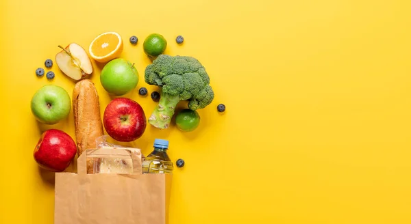 Shopping paper bag full of healthy food on yellow background. Flat lay with copy space