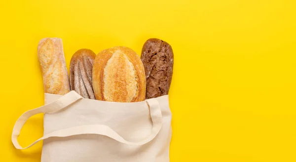 Fresh baked bread in bag on yellow background. Flat lay with copy space