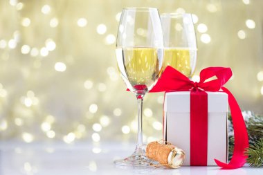 Şampanya bardakları ve hediye kutuları Noel ışıklarının önünde.