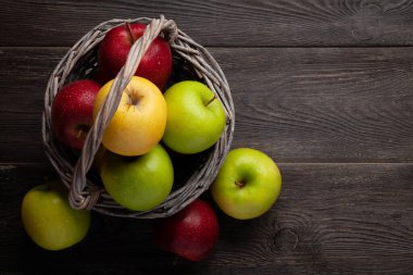 Tahta masada sepetin içinde renkli olgun elma meyveleri. Üst görünüm düzlüğü kopyalama alanı ile yatıyordu