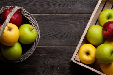 Sepette renkli olgun elma meyveleri ve tahta masada kutu. Üst görünüm düzlüğü kopyalama alanı ile yatıyordu