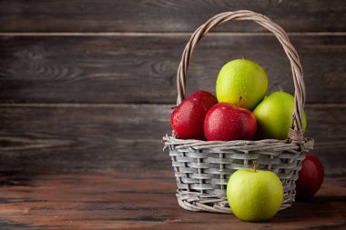 Tahta masada sepetin içinde renkli olgun elma meyveleri. Kopyalama alanı ile
