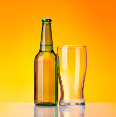 Sarı arka planda bira şişesi ve boş bardak. Stüdyo çekimi