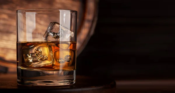 ウイスキー コニャックまたは黄金のラム酒と氷とガラス コピースペースと古い木製の樽の前で — ストック写真