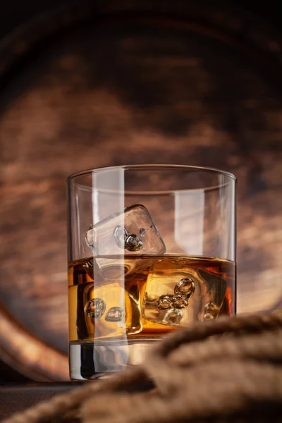 ウイスキー コニャックまたは黄金のラム酒と氷とガラス コピースペースと古い木製の樽の前で — ストック写真