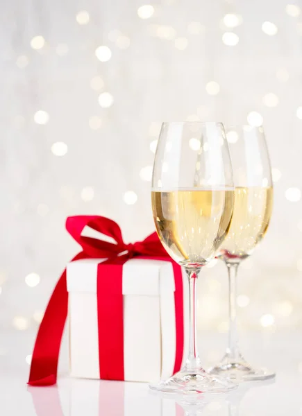 Champagne glasses and gift box in front of Christmas lights bokeh