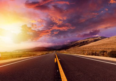 Kırsal alanda, gün batımında dramatik gökyüzü ile boş asfalt yol