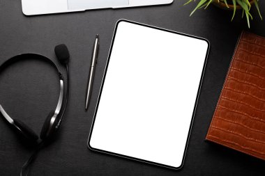 Masasında boş ekran, kulaklık ve ofis malzemeleri olan bir tablet. Üst görünüm düzlüğü kopyalama alanı ile yatıyordu