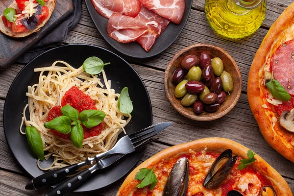 Italian cuisine. Pasta, pizza, olives and antipasto toasts. Flat lay on wooden table