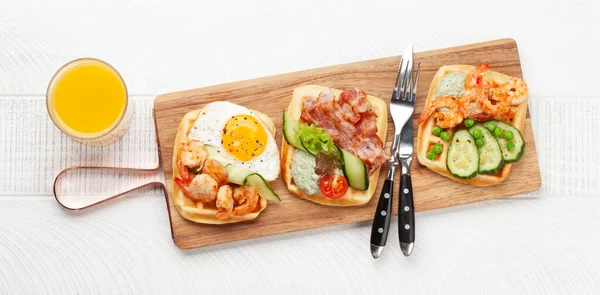 Breakfast waffles with fried eggs, salmon, bacon, cucumber and prawns. Top view flat lay with copy space