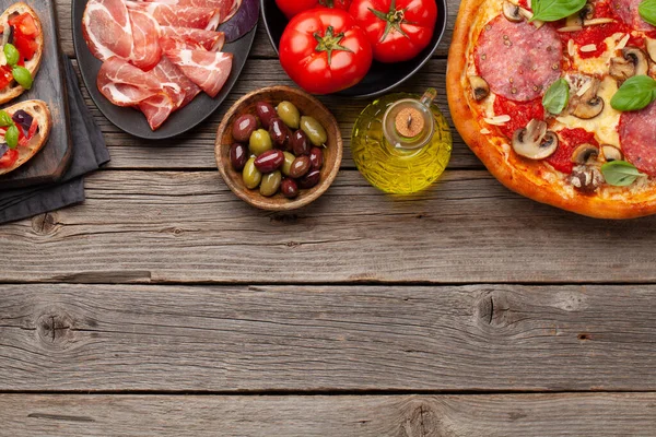 Italian cuisine. Pepperoni pizza and antipasto toasts. Flat lay on wooden table with copy space