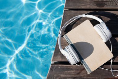 Yüzme havuzunun yanında kitap ve kulaklık. Yaz tatili. Kopyalama alanı olan düz