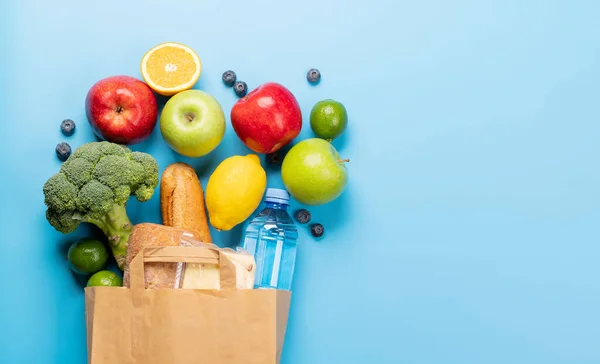 Shopping paper bag full of healthy food on blue background. Flat lay with copy space