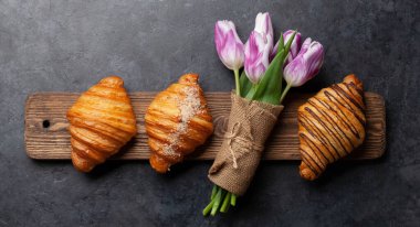 Tahta tahtada çeşitli kruvasanlar ve lale buketi. Fransız kahvaltısı. Üst görünüm düzlüğü