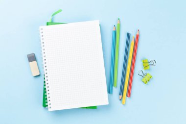 Boş not defteri ve renkli kalemler var. Fotokopi alanı ile mavi arkaplan üzerinde düz yatıyordu