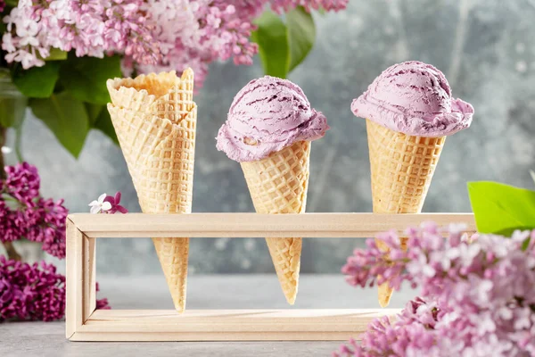Berry ice cream sundae in waffle cones and lilac flowers