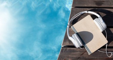 Yüzme havuzunun yanında kitap ve kulaklık. Yaz tatili. Kopyalama alanı olan düz