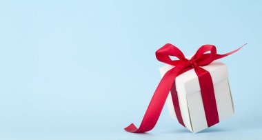 Mavi arka planda kırmızı kurdeleli beyaz hediye kutusu. Noel, doğum günü ya da sevgililer günü için yer var mı?