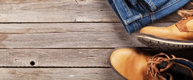 Erkek kıyafetleri ve aksesuarları. Ahşap arka planda kot pantolon ve ayakkabılar. Üst görünüm düzlüğü kopyalama alanı ile yatıyordu