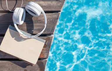 Yüzme havuzunun yanında kitap ve kulaklık. Yaz tatili. Kopyalama alanı olan düz