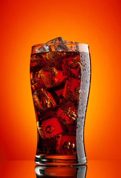 Cola with ice. Fresh cold sweet drink with ice cubes. Over red background