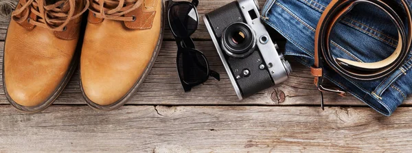 Men\'s clothes and accessories. Jeans, shoes, glasses, camera on wooden background. Top view flat lay