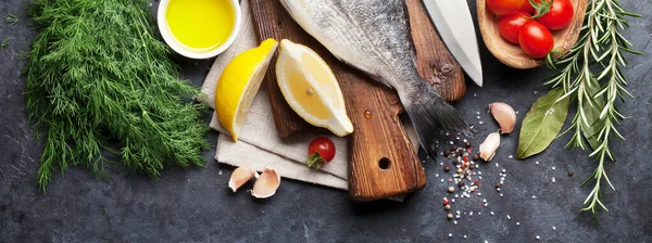 Raw fish cooking and ingredients. Dorado, lemon, herbs and spices. Flat lay on stone table
